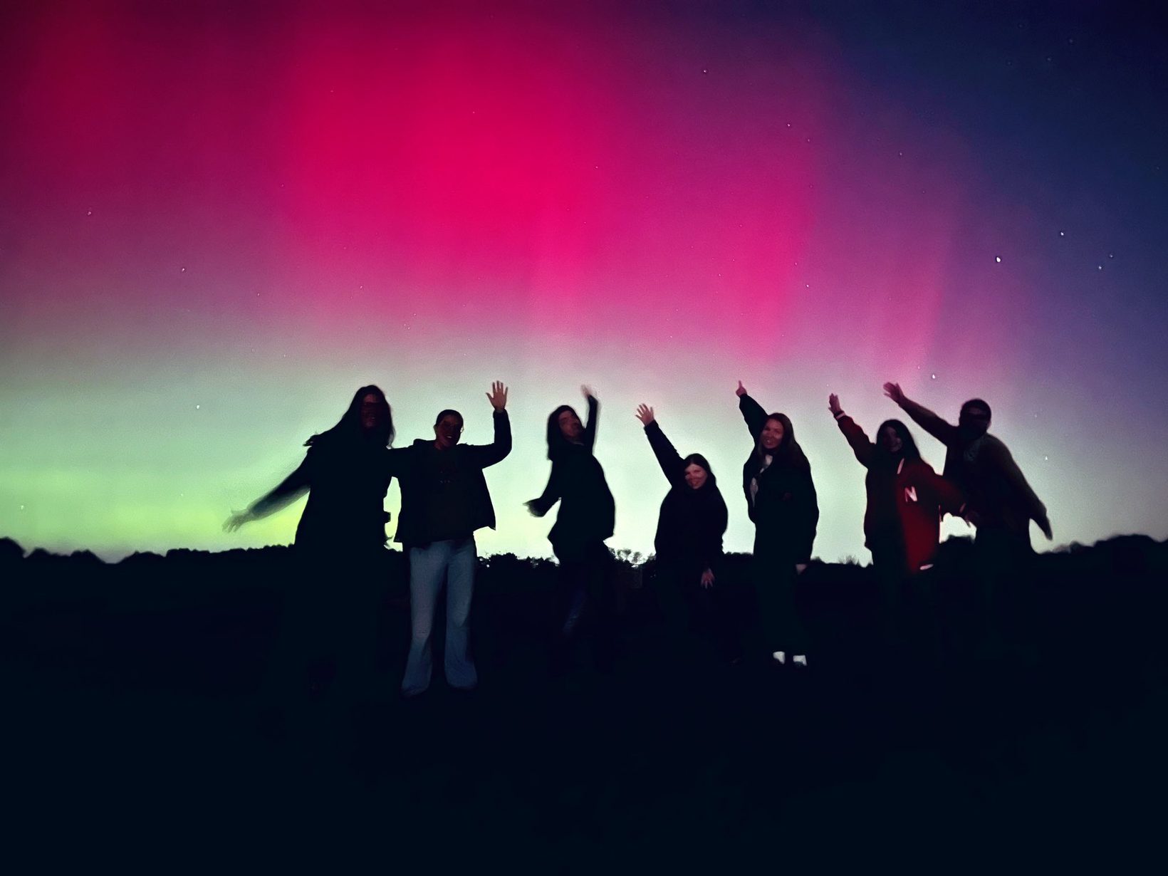 A group of people silhouetted against a bright pink and green aurora during the May 2024 geomagnetic storm